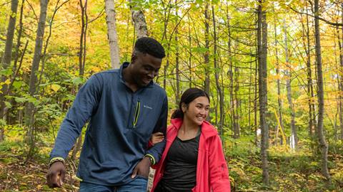 Two people walking and smiling through a forest in autumn.