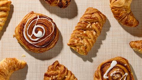 Assorted pastries on a woven mat, including croissants and cinnamon swirls with icing.