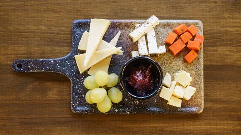 An assortment of cheeses served with grapes and jam on a rectangular serving board.