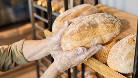 Person in gloves placing freshly baked bread on wooden shelves.