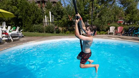 A boy joyfully swinging on a rope above a swimming pool on a sunny day, about to splash into the water.