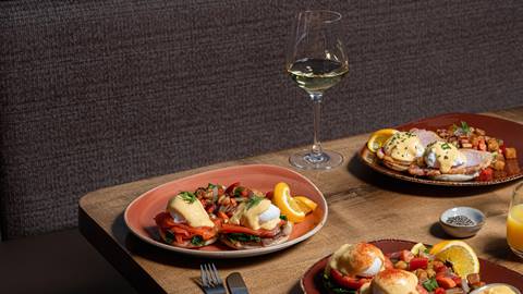 A gourmet breakfast spread with eggs benedict and poached eggs on colorful plates, accompanied by a glass of white wine.