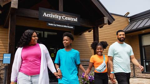 A family of four happily walking past "activity central," a building offering walk-up tickets and bike rentals.