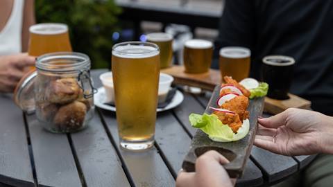 People dining outdoors, sharing food and drinks including beer and appetizers on a wooden table.