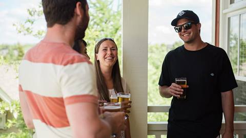 Group of friends enjoying a conversation and drinks on a sunny balcony.