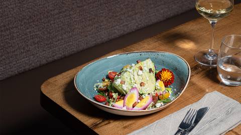 Gourmet salad served on a blue plate with a glass of white wine on a wooden table.