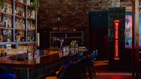 Dimly lit bar with neon sign and array of bottles on shelves.