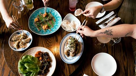 People dining at a wooden table with a variety of asian dishes.