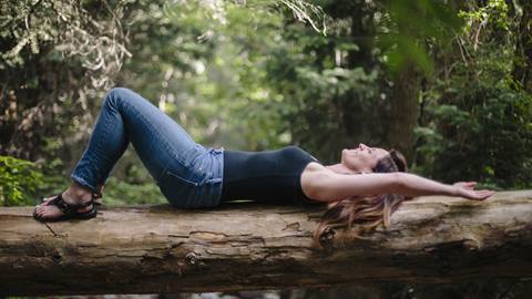 Woman reclining on a fallen tree in a forest setting.