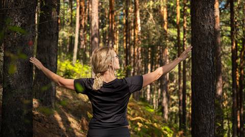 Woman with arms outstretched enjoying the serenity of a forest.