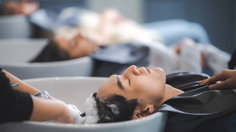 Young man pampering himself at salon with hair spa, hair cut and hair wash in salon with professional hair stylist in modern salon with eyes closed