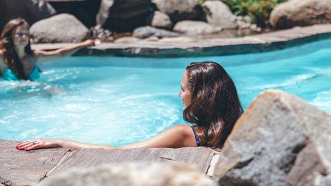 Two individuals relaxing by the side of a swimming pool on a sunny day.
