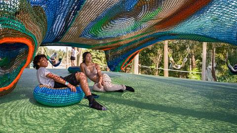 two youth sitting on crocheted seats under the cocoon crawl playground climbing net at blue mountain