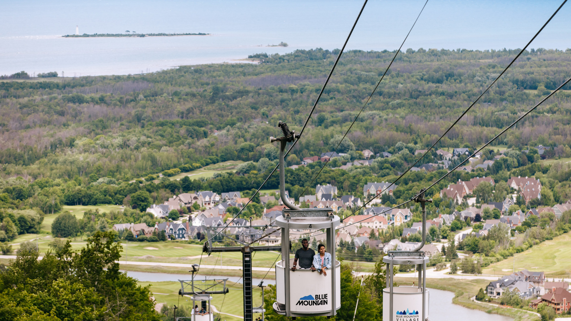 Couple riding Gondola at Blue Mountain with view of Georgian Bay in background