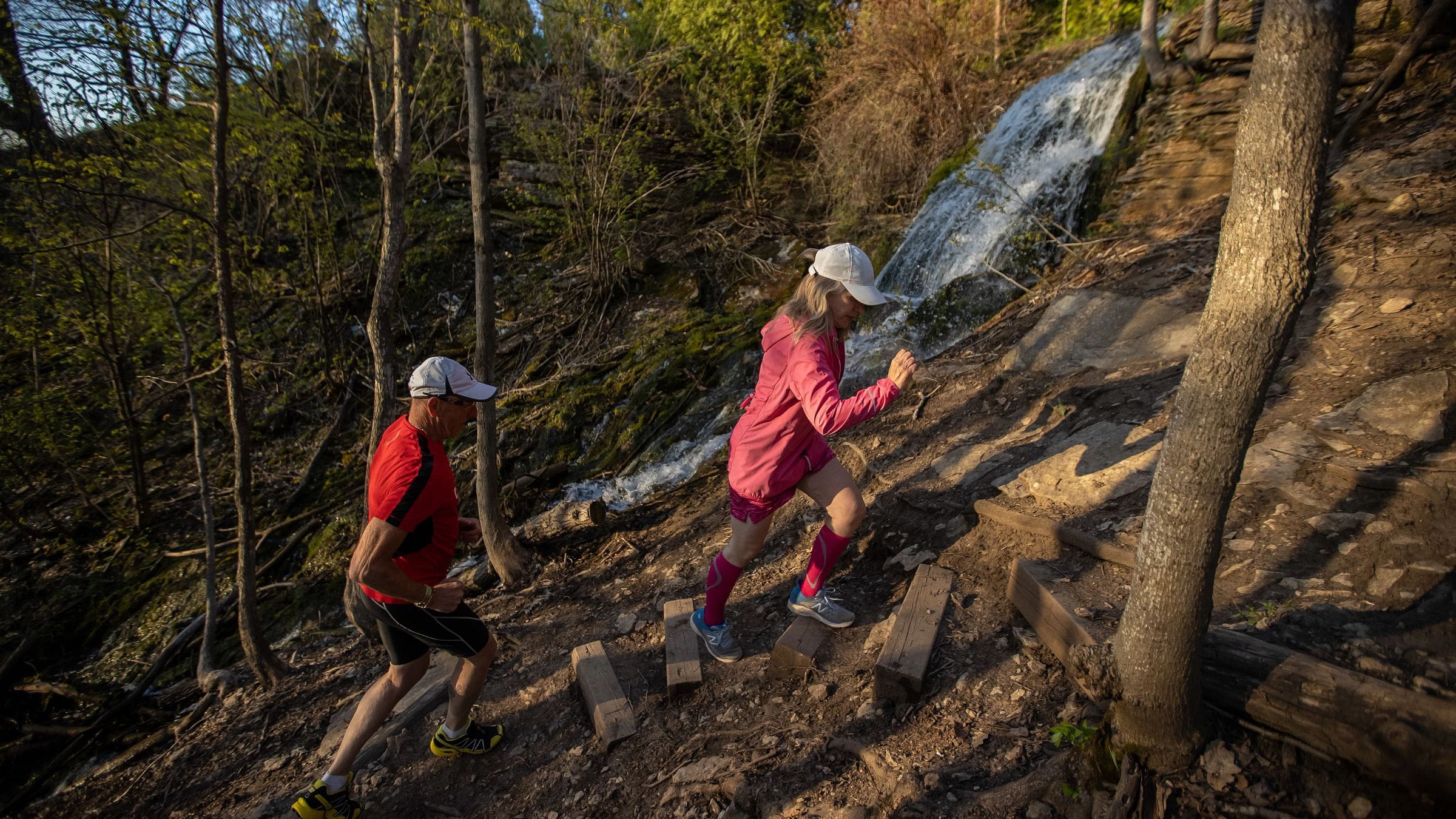 Pair of joggers running up Blue Mountain Explore Park trail past a waterfall