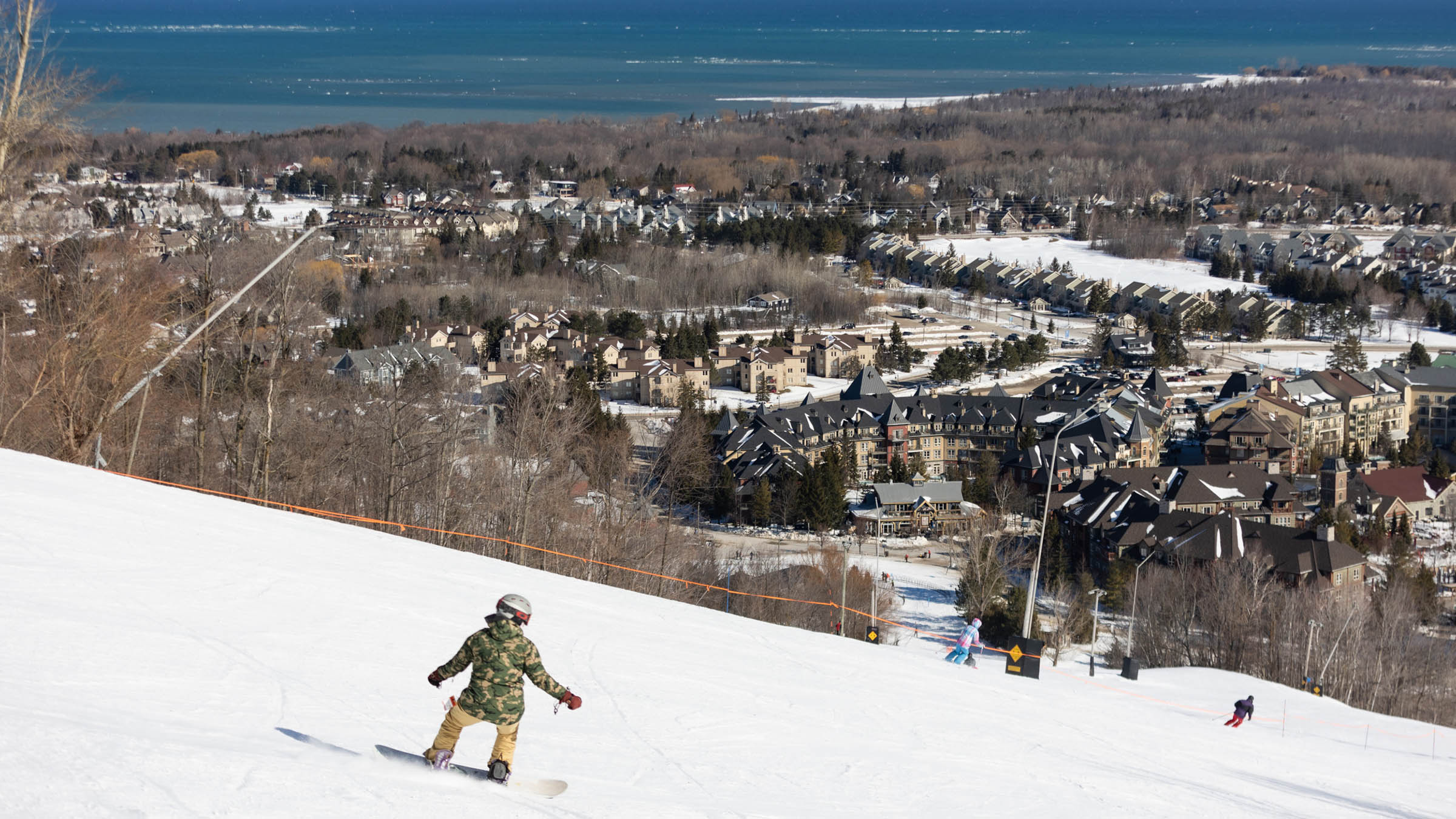 Person riding down the run at Blue Mountain with Hotels in the background during Winter Fix Stay and Ski Deal. 