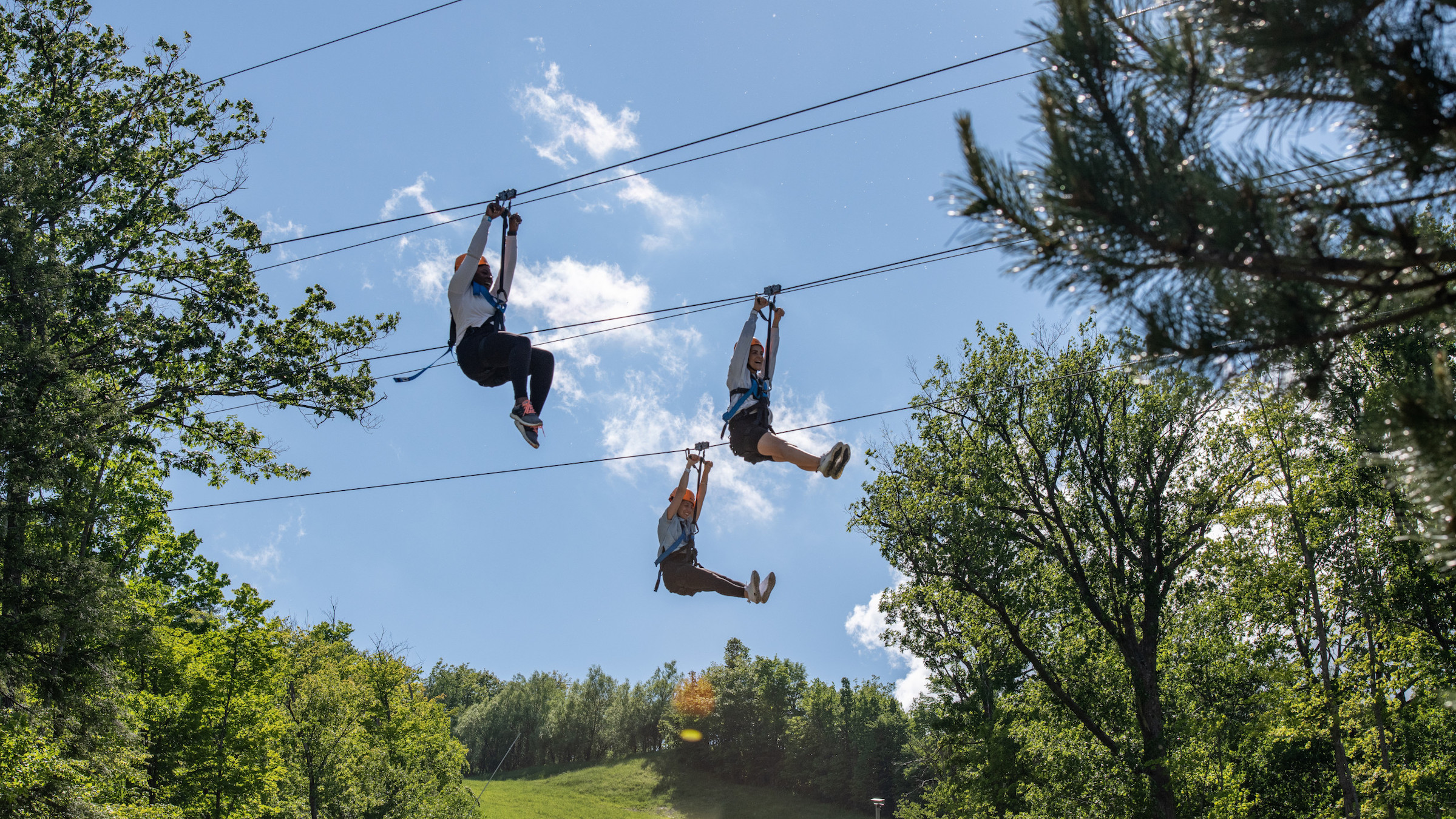 Three people riding down the ziplines on Blue Mountain's Wind Rider Triple Zips