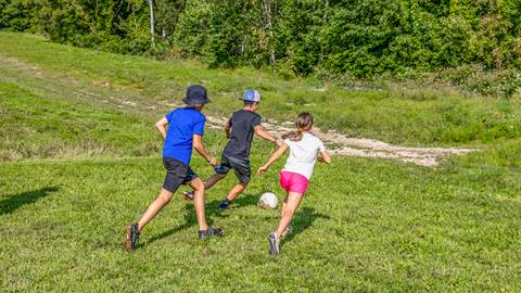 Three children running up a grassy hill, playing soccer at Blue Mountain Resort Summer camps 