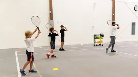 Tennis instructor guiding young players during an indoor practice session.