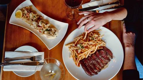 A hand holding a piece of fries, with food on a table