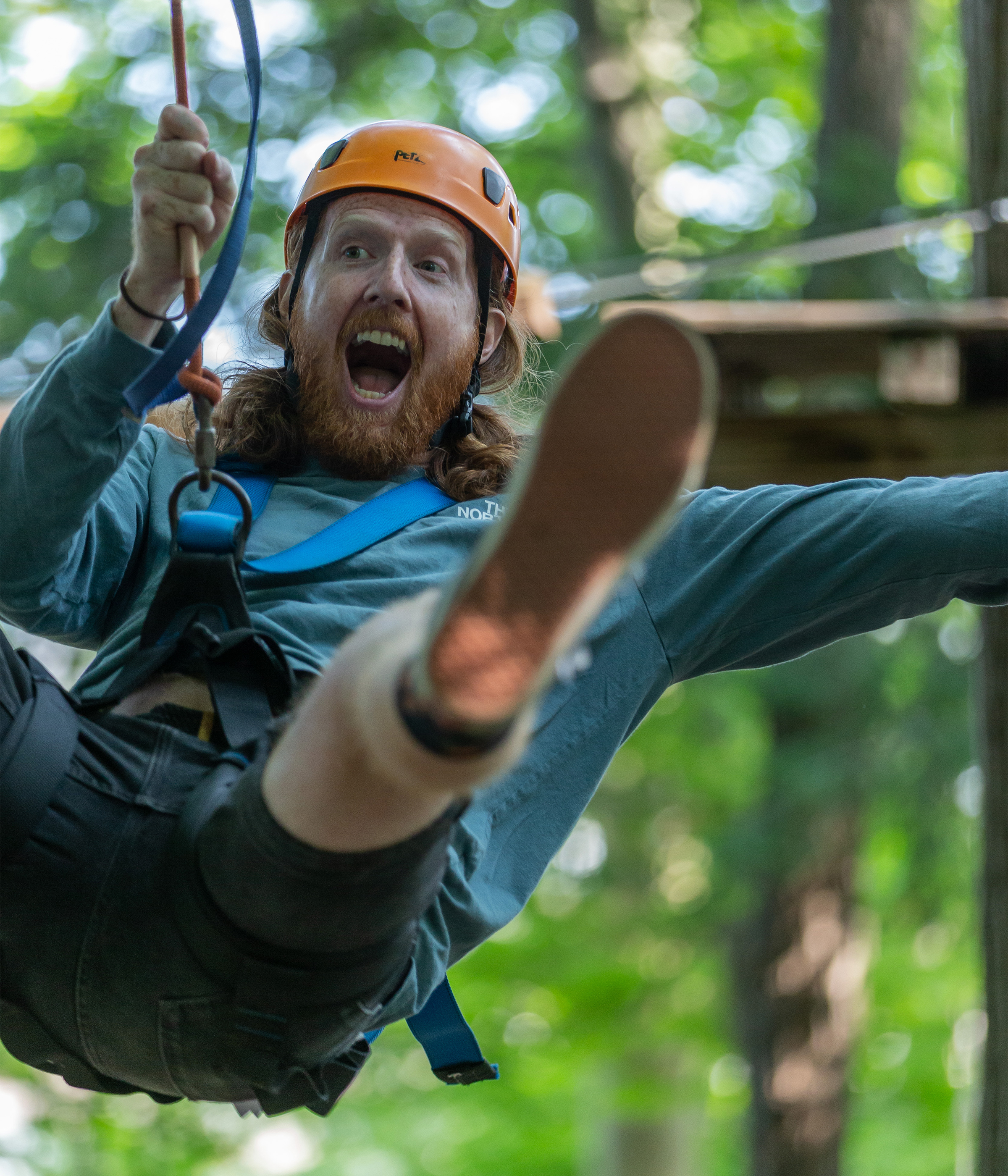 Man with a surprised expression enjoying a zip line adventure through a forest.