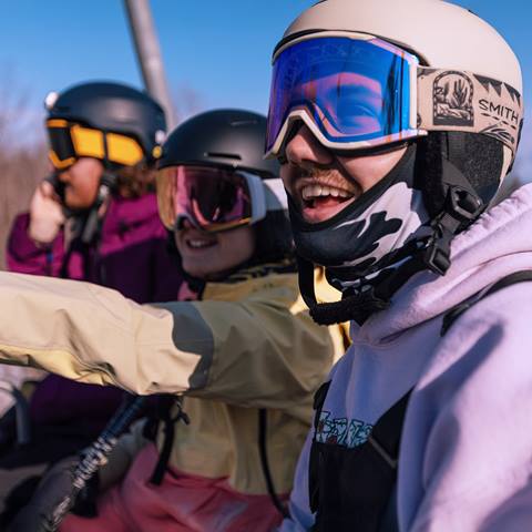 Three people (two happy and one on their phone) sitting on a chairlift.