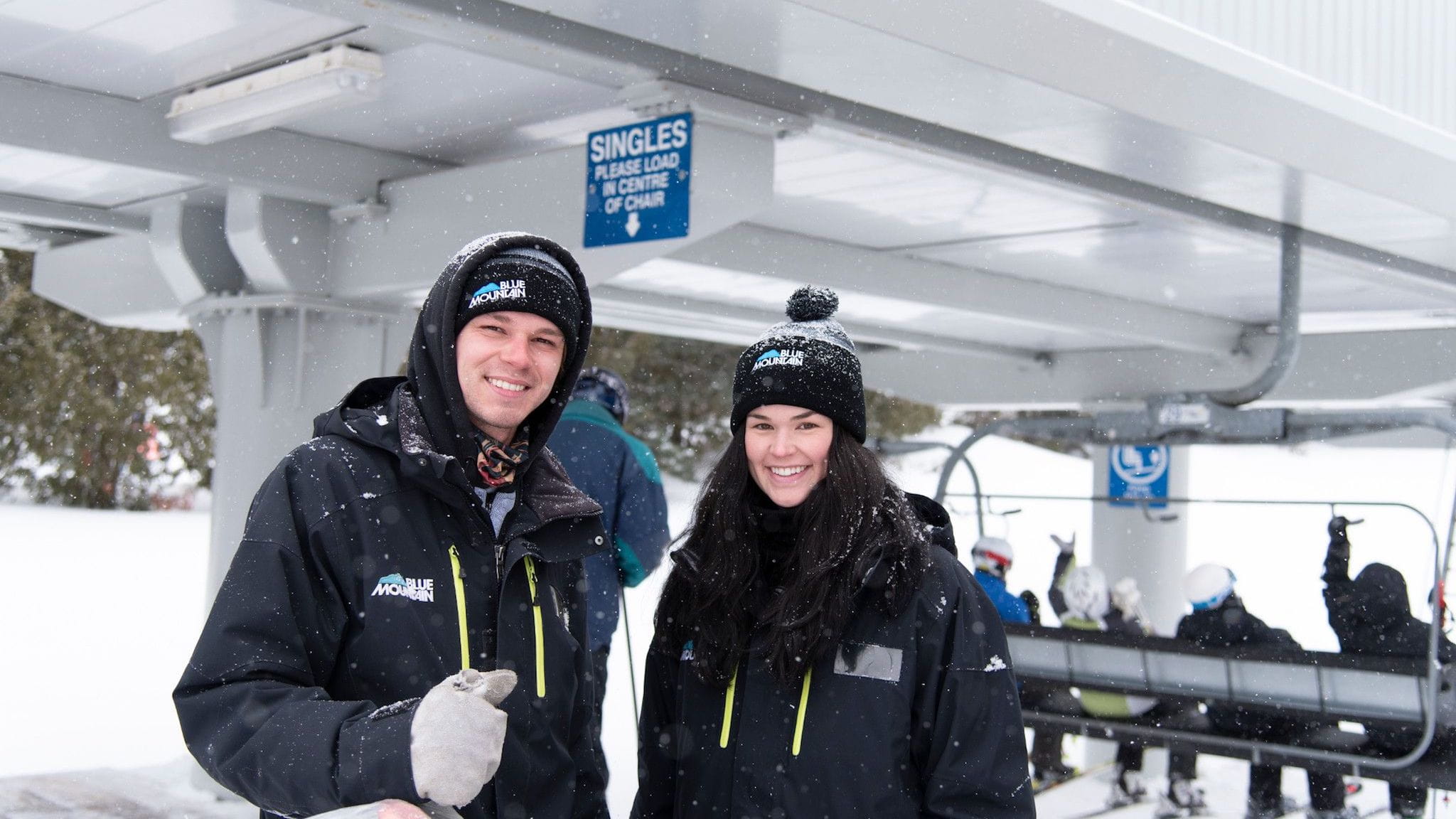 Two Blue Mountain Employees standing in front of lift with riders sitting on chair
