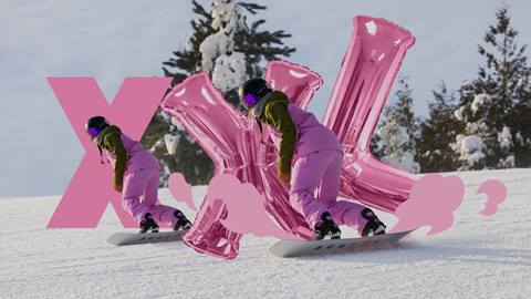 A snowboarder in pink gear rides down a snowy slope. Pink inflatable letters "XXL" and snow-covered trees are in the background.