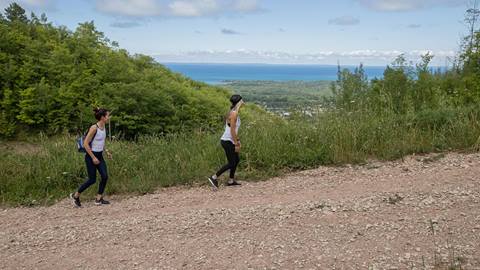 two people walking uphill a multi-use trail with a view of the coast at blue mountain resort