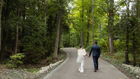 Bride and groom walking along path through forest at Blue Mountain Resort