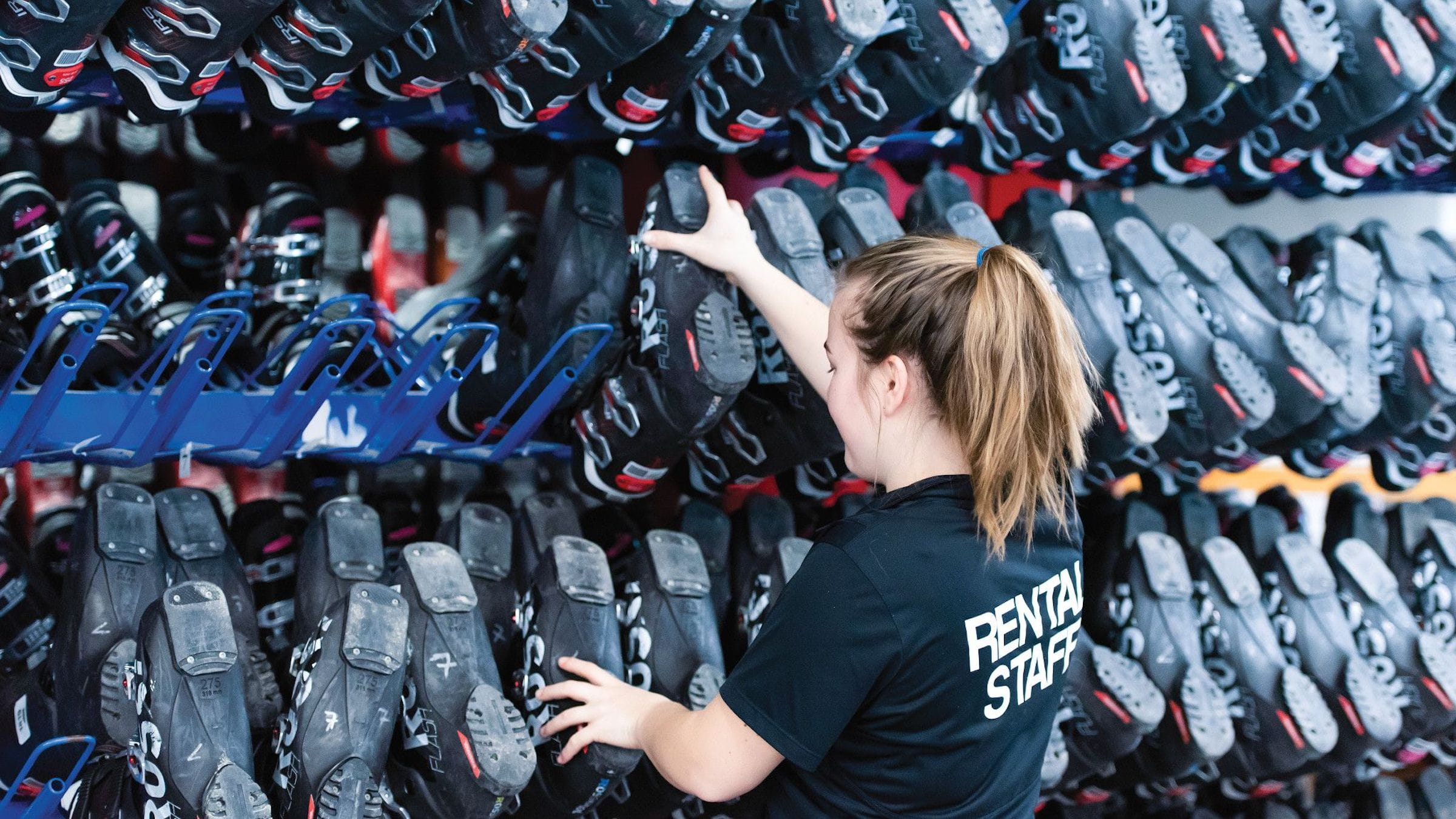 Ski boots on rack with blue mountain rental staff placing boots back up