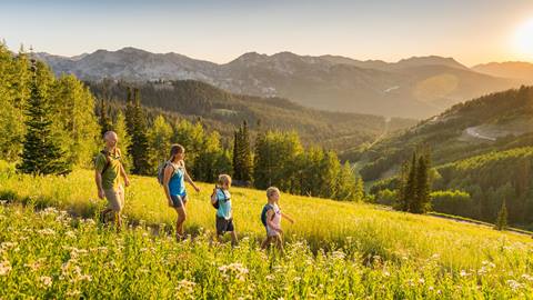 Family hiking through grass field with sunset in background